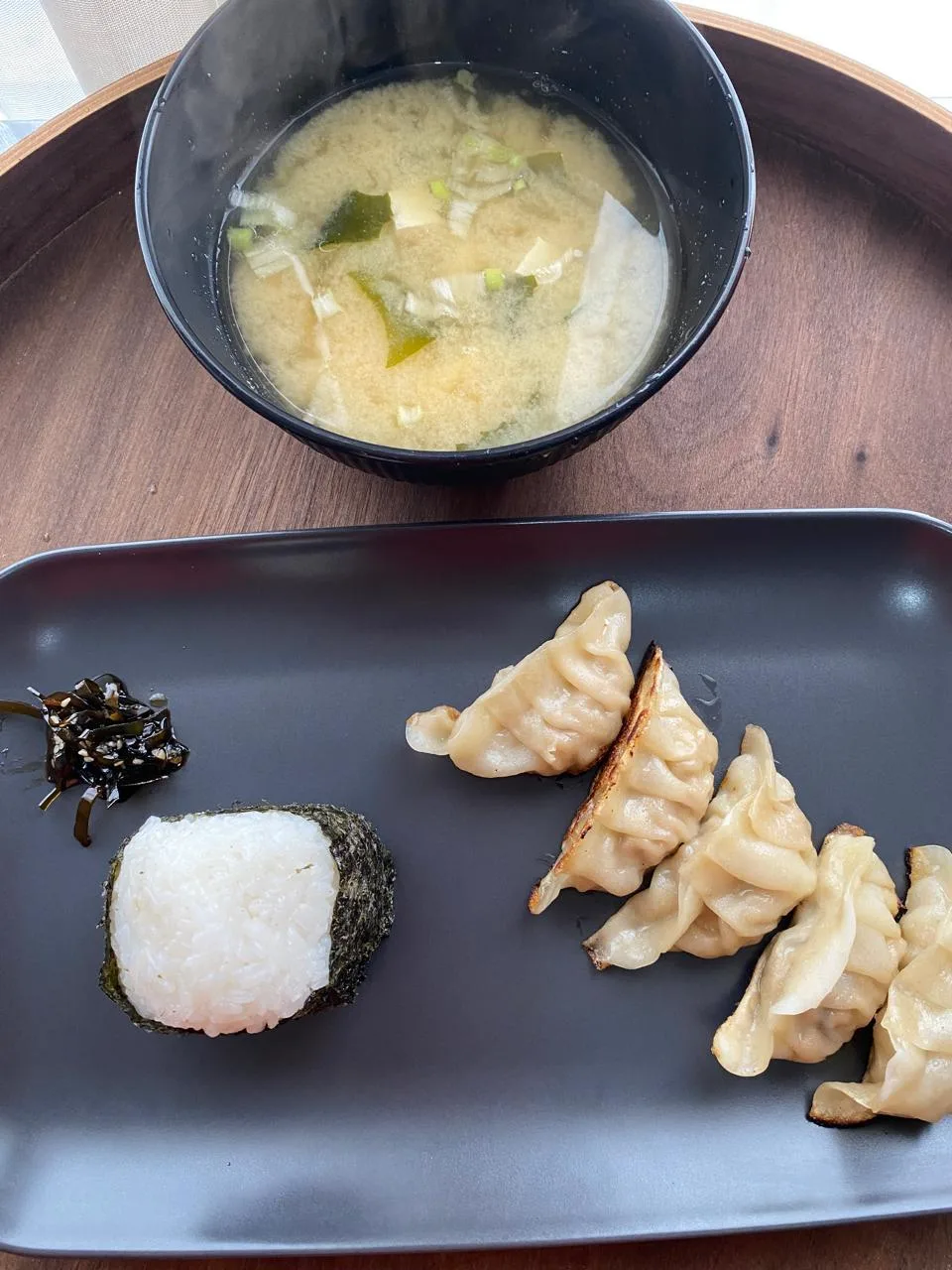 Combo servido: sopa miso, un onigiri y cinco gyozas en un plato negro