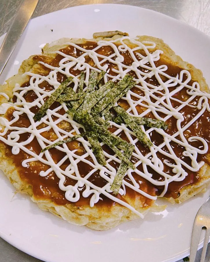 Okonomiyaki cubierto de salsa, hilos de mayonesa y tiras de alga nori